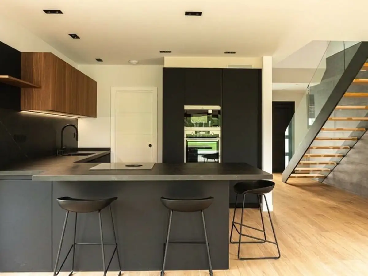 Cocina en negro con isla y escalera de cristal al fondo en Urbanización La Solana